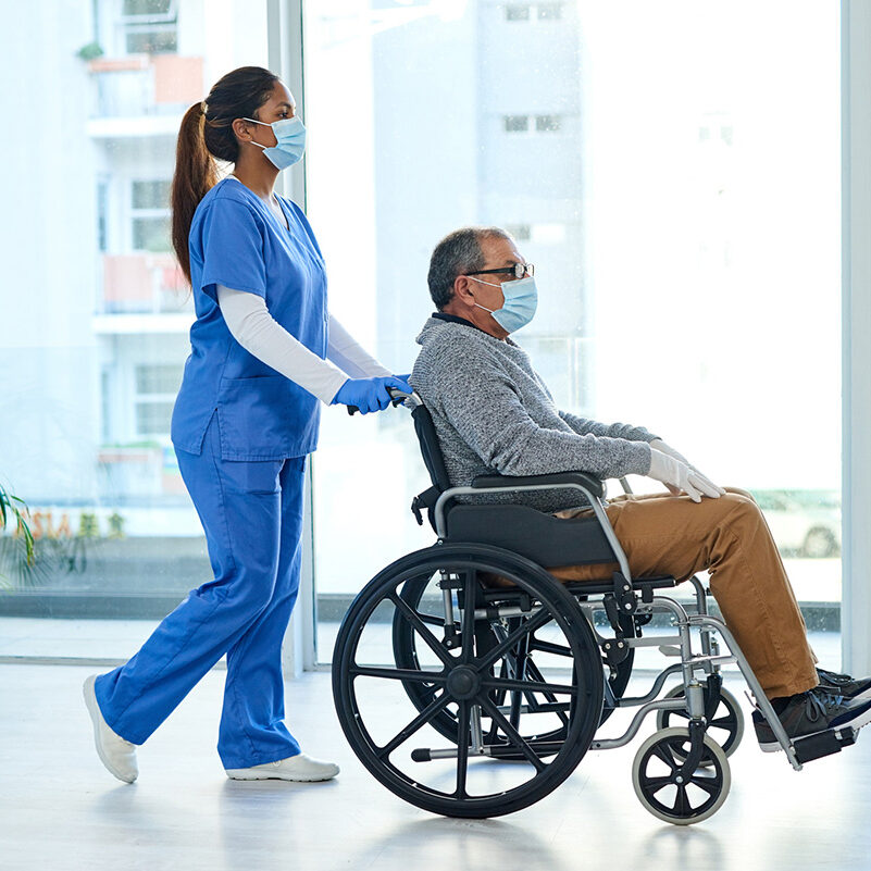 Shot of a masked young nurse pushing a senior man in a wheelchair